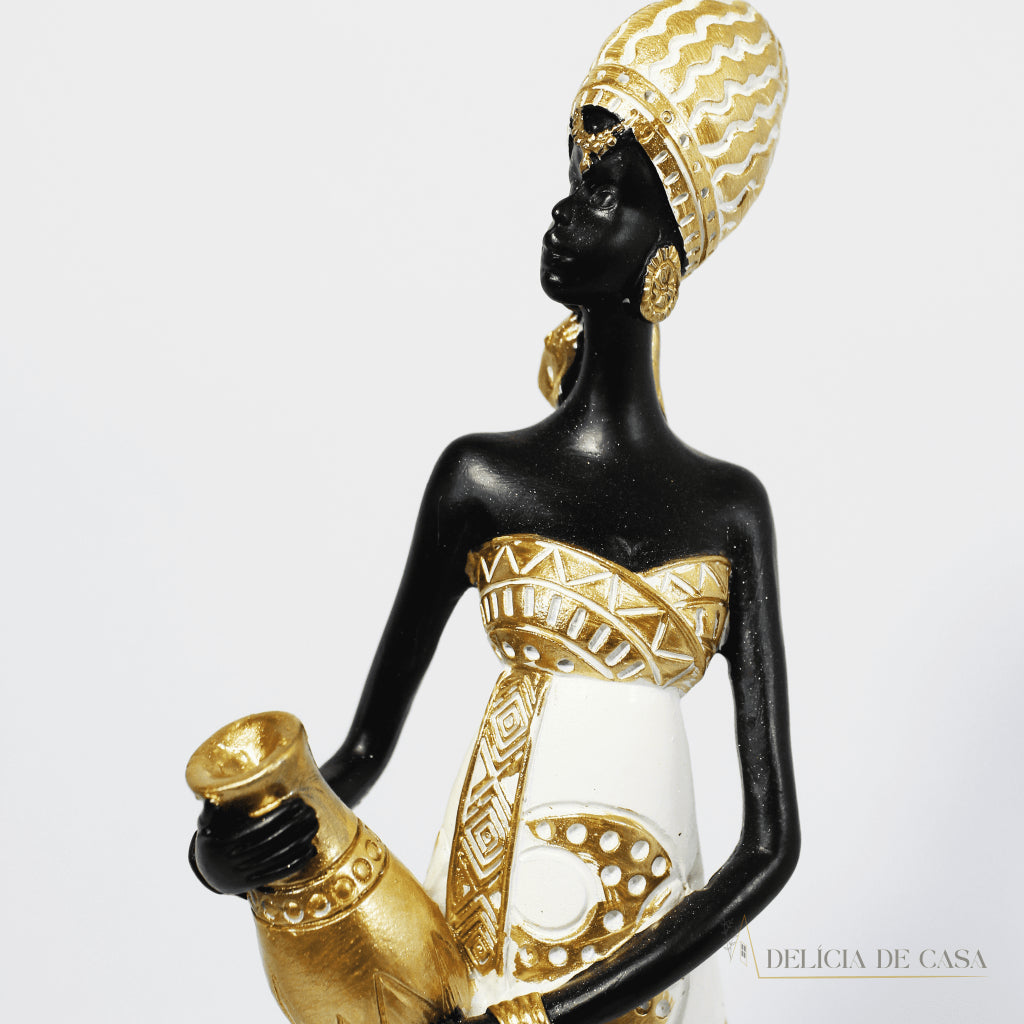 Estátua decorativa de mulher africana em resina nas cores branco, dourado e preto, com trajes típicos, medindo 32,5 cm de altura — peça elegante e cultural para decoração de interiores.