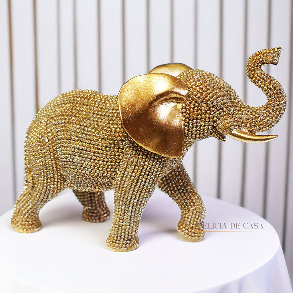 Escultura de elefante dourado coberto de strass, com tromba erguida e detalhes refinados, ideal para decoração luxuosa.