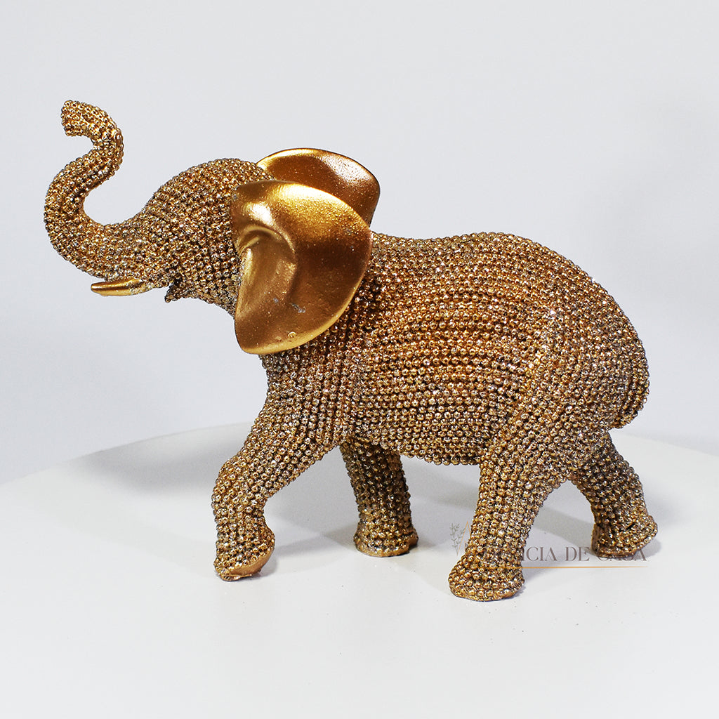 Escultura de elefante dourado coberto de strass, com tromba erguida e detalhes refinados, ideal para decoração luxuosa.
