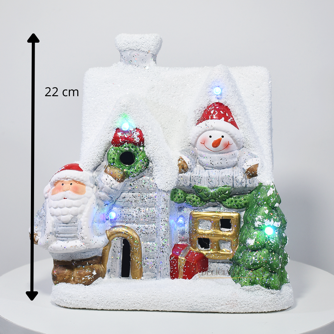 Casinha decorativa de Natal com Papai Noel, boneco de neve e árvore, feita em resina com glitter e luzes coloridas, 22 cm de altura.