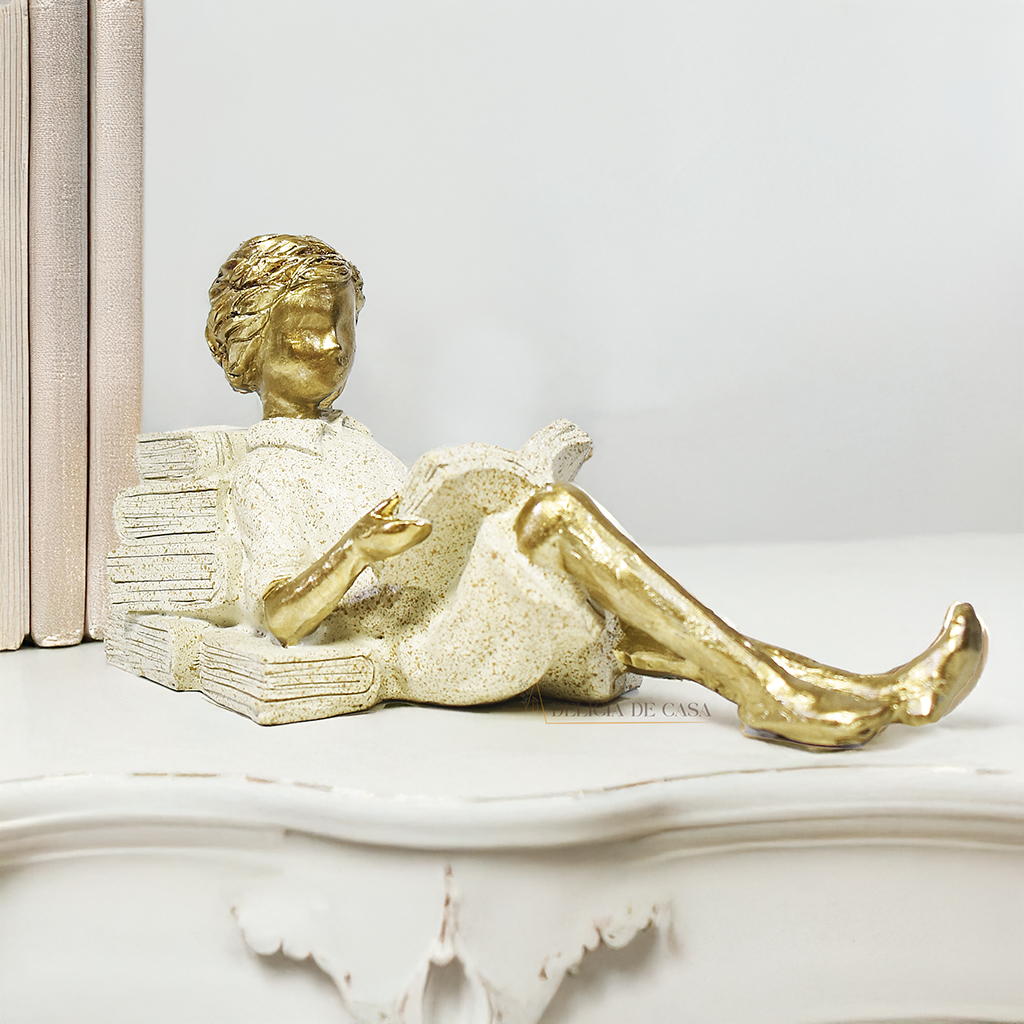 Escultura decorativa de menino lendo, deitada com as pernas cruzadas, feita em resina dourada Decoração para apaixonados por livros.