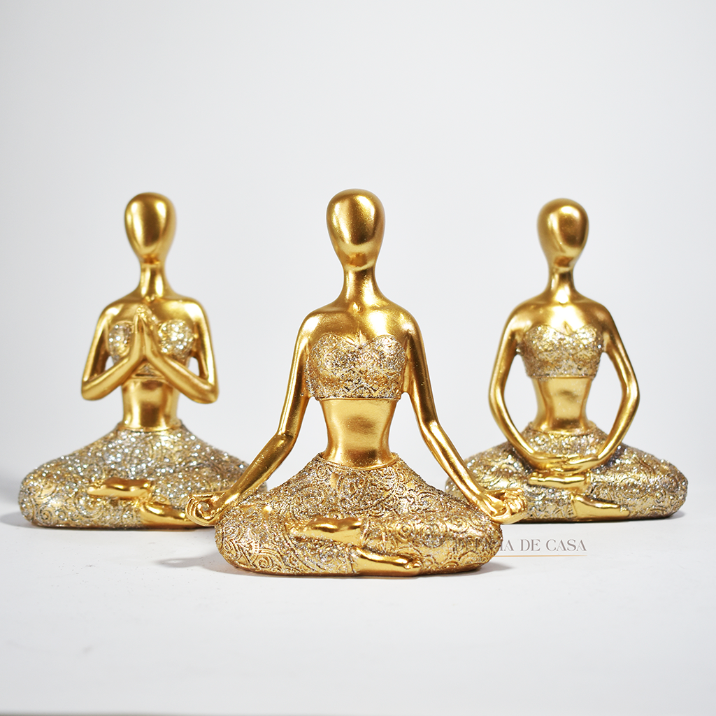 Trio de estátuas douradas com glitter representando posturas de ioga, ideal para decoração zen e ambientes de meditação.