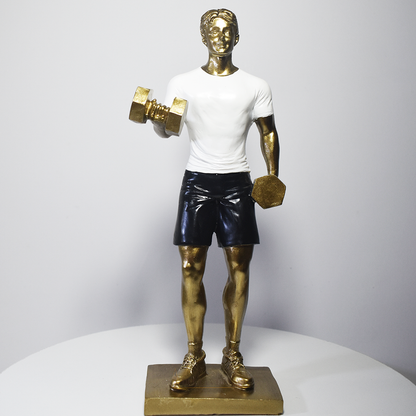 Escultura decorativa em resina representando atleta realizando exercício com halteres, com acabamento dourado, camiseta branca e shorts pretos.