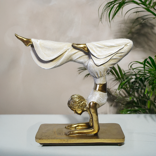 Escultura decorativa em resina de mulher praticando yoga em posição de equilíbrio, com acabamento dourado e branco perolado.