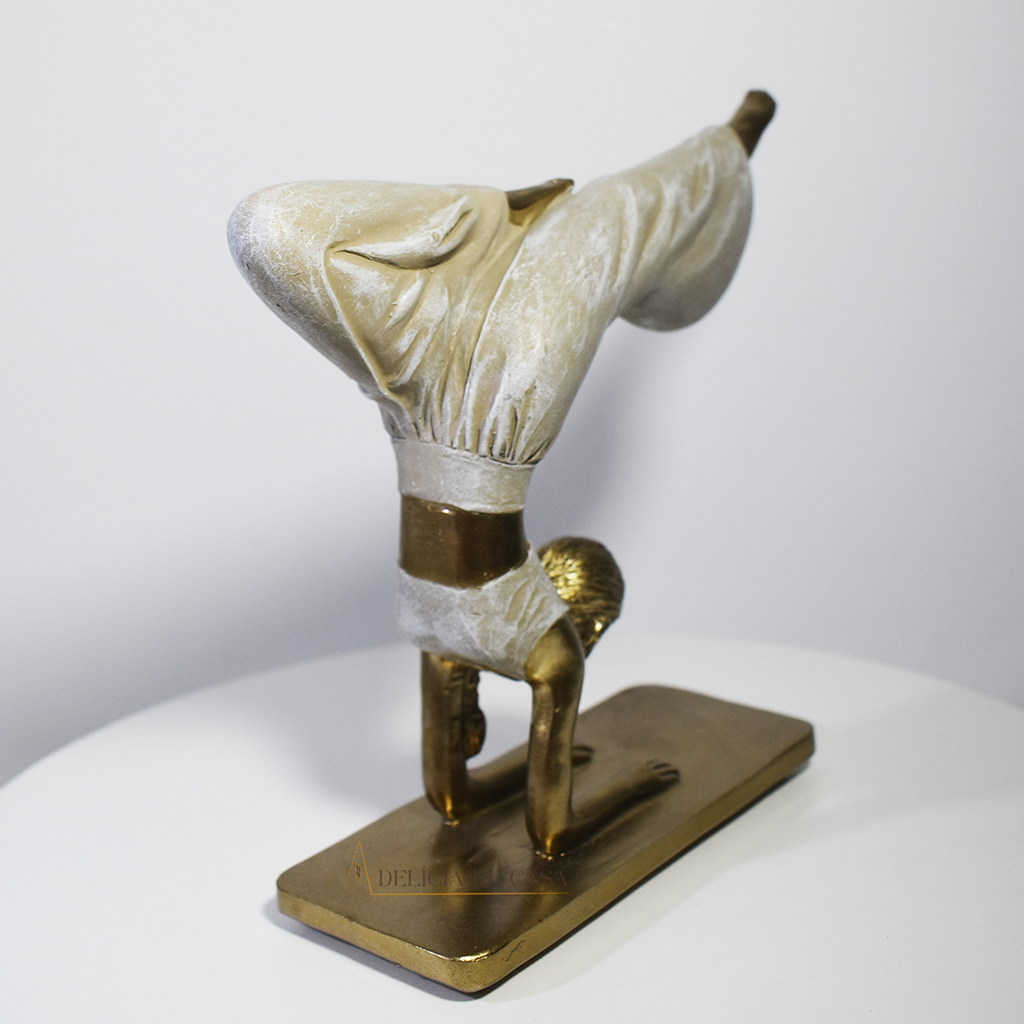 Escultura decorativa em resina de mulher praticando yoga em posição de equilíbrio, com acabamento dourado e branco perolado.