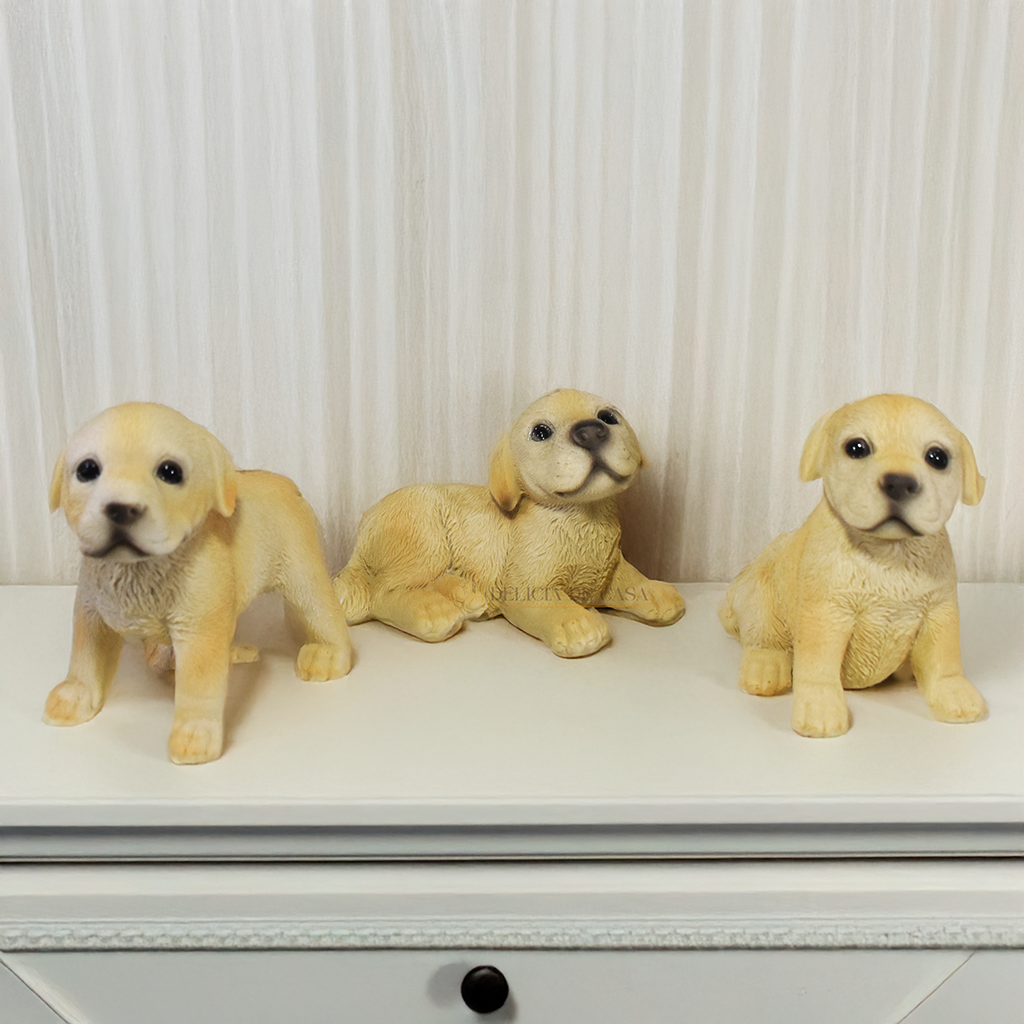 Três enfeites decorativos de cachorro Labrador em resina nas posições deitado, em pé e sentado sobre superfície branca
