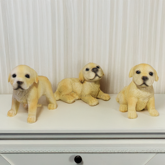 Três enfeites decorativos de cachorro Labrador em resina nas posições deitado, em pé e sentado sobre superfície branca