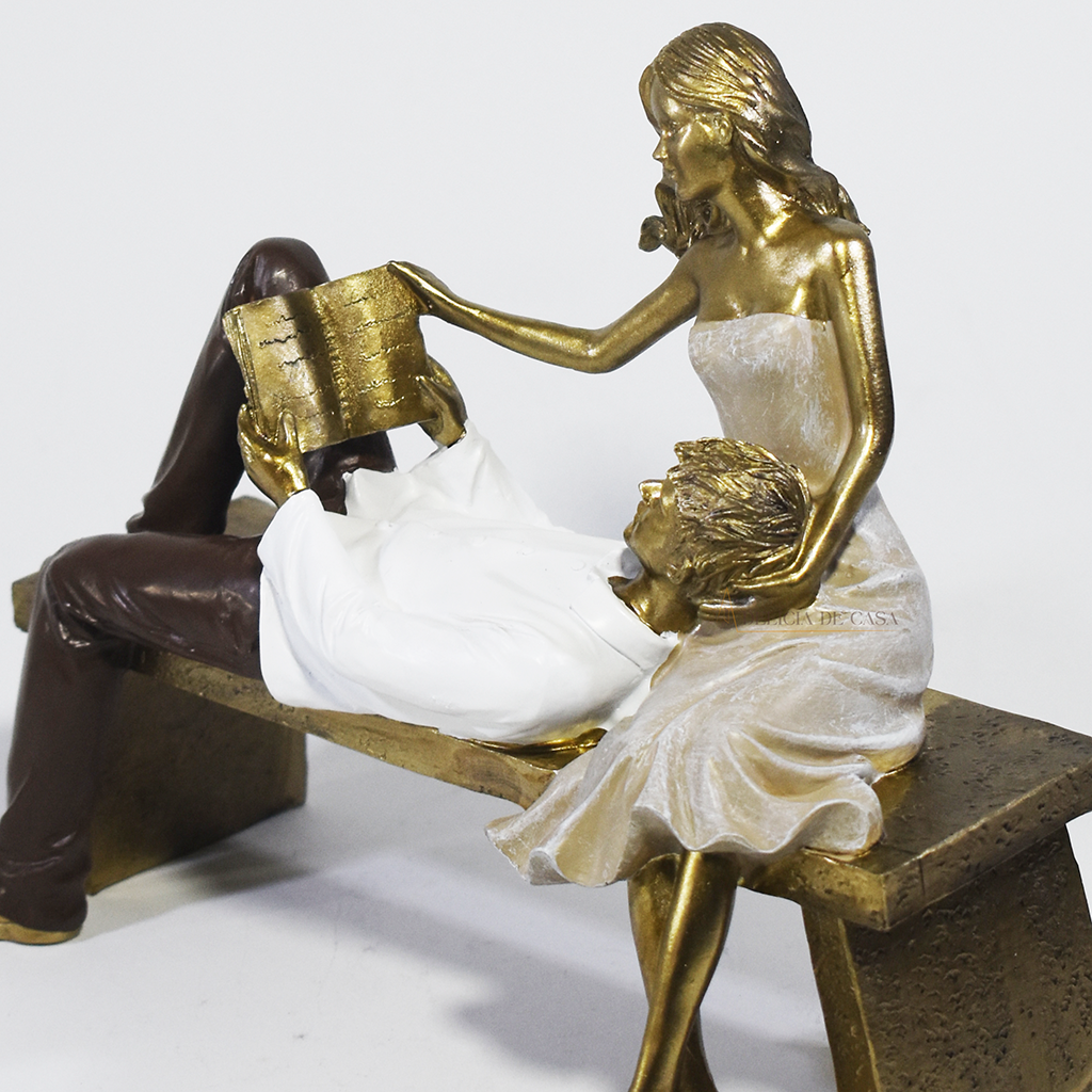 Escultura decorativa de casal romântico em resina sentados em um banco, com acabamento dourado, branco e marrom, simbolizando amor, cumplicidade e momentos especiais. 22,5x13x18 cm.