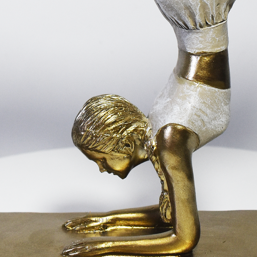 Escultura decorativa em resina de mulher praticando yoga em posição de equilíbrio, com acabamento dourado e branco perolado.