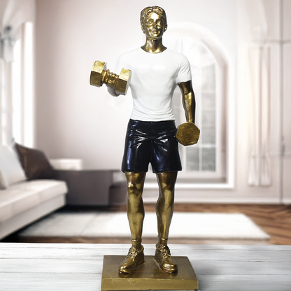 Escultura decorativa em resina representando atleta realizando exercício com halteres, com acabamento dourado, camiseta branca e shorts pretos.