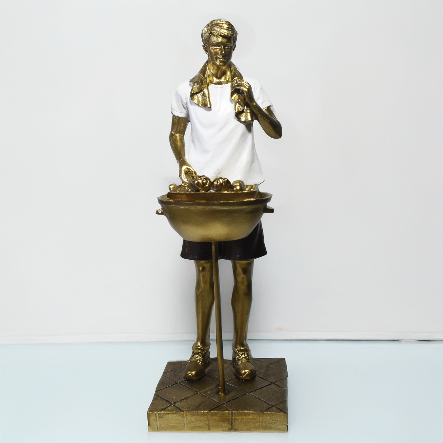 Escultura decorativa em resina de churrasqueiro ao lado de uma churrasqueira, com acabamento dourado, branco e preto.