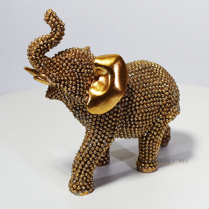 Escultura de elefante dourado coberto de strass, com tromba erguida e detalhes refinados, ideal para decoração luxuosa.