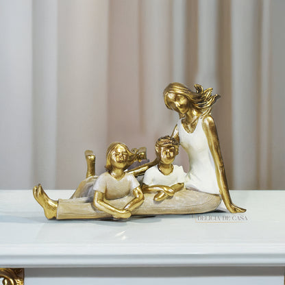 Escultura decorativa de mãe com dois filhos sentados, em resina dourada e branca, representando amor e união familiar.