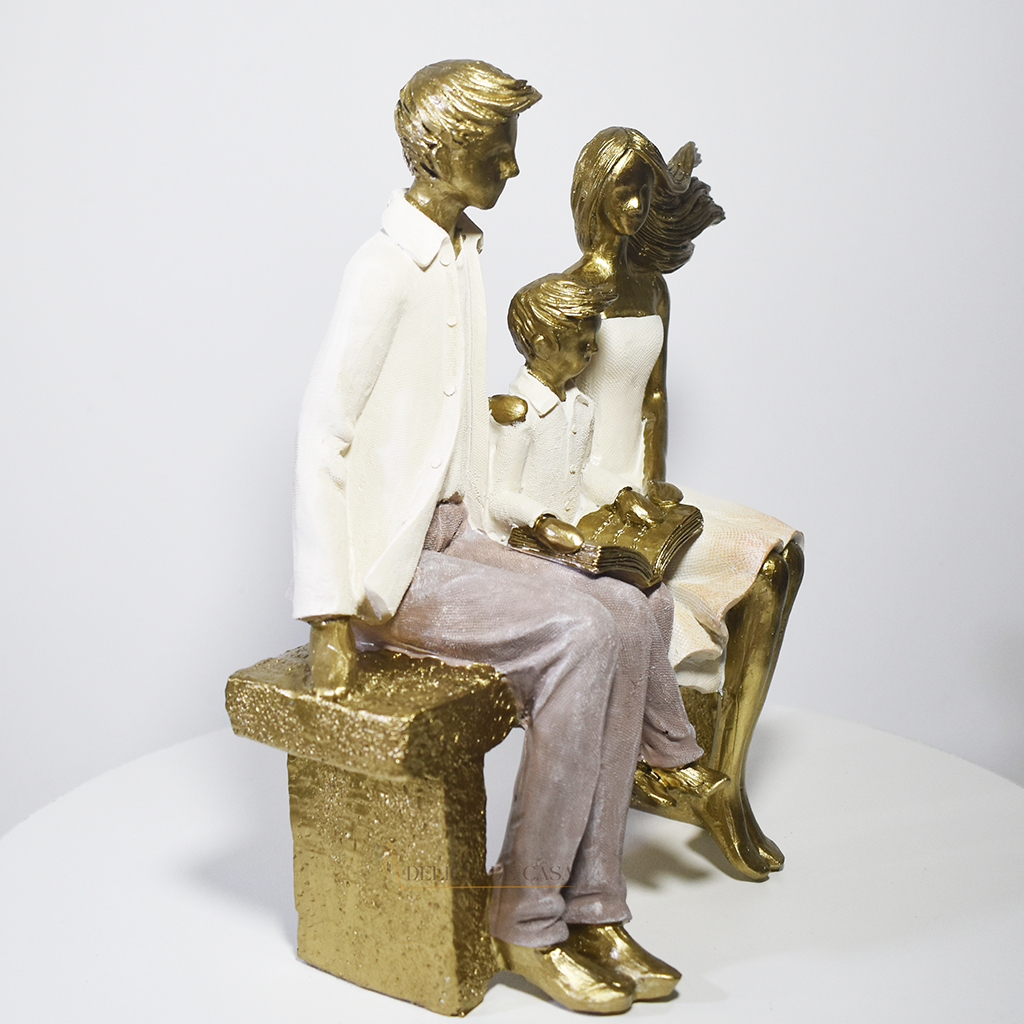 Escultura decorativa em resina representando pai, mãe e filho sentados em um banco lendo um livro, simbolizando união familiar e momentos de aprendizado.