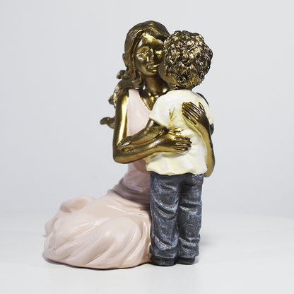 Escultura decorativa de mãe abraçando seu filho, confeccionada em resina com acabamento dourado, branco e cinza, medindo 11,5 x 11,5 x 8 cm.