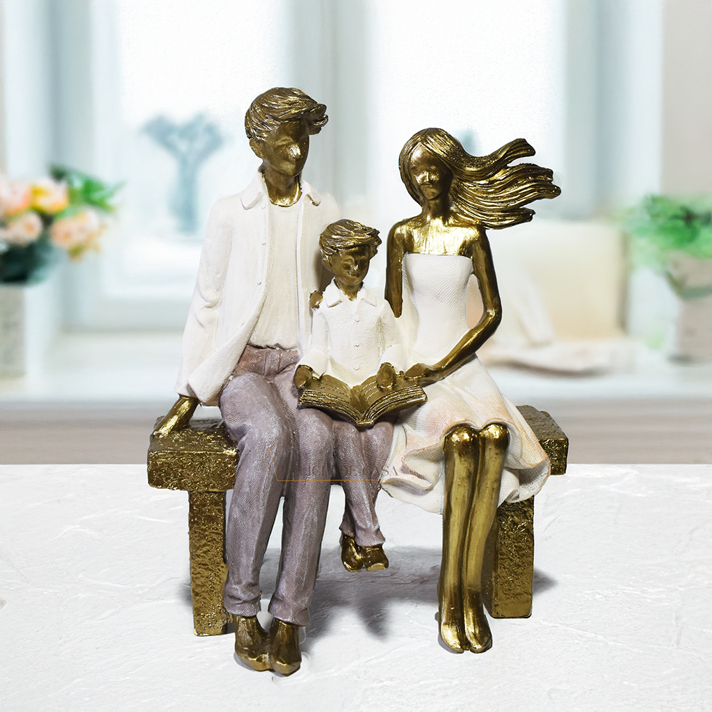Escultura decorativa em resina representando pai, mãe e filho sentados em um banco lendo um livro, simbolizando união familiar e momentos de aprendizado.