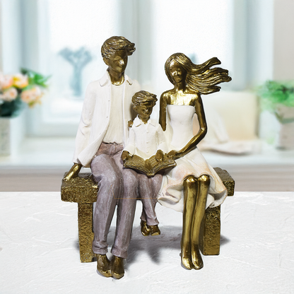 Escultura decorativa em resina representando pai, mãe e filho sentados em um banco lendo um livro, simbolizando união familiar e momentos de aprendizado.