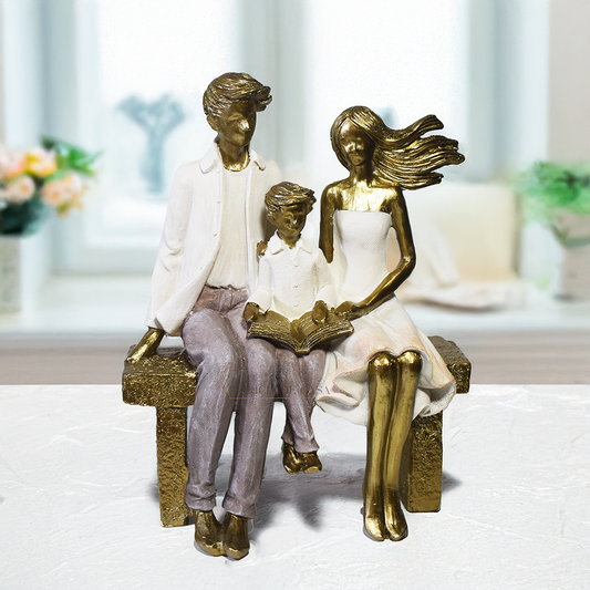 Escultura decorativa em resina representando pai, mãe e filho sentados em um banco lendo um livro, simbolizando união familiar e momentos de aprendizado.