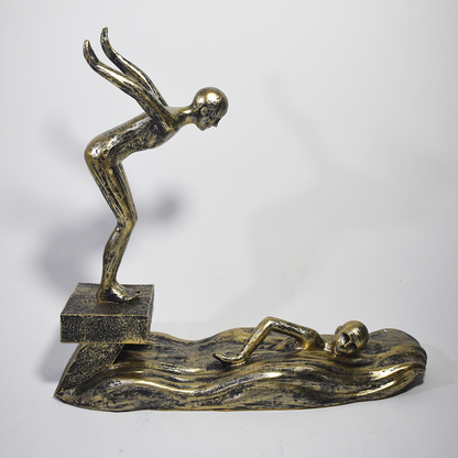 Escultura decorativa em resina representando atletas da natação, com um mergulhador e um nadador sobre ondas estilizadas em acabamento dourado envelhecido.