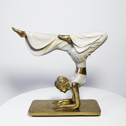 Escultura decorativa em resina de mulher praticando yoga em posição de equilíbrio, com acabamento dourado e branco perolado.