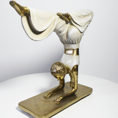 Escultura decorativa em resina de mulher praticando yoga em posição de equilíbrio, com acabamento dourado e branco perolado.