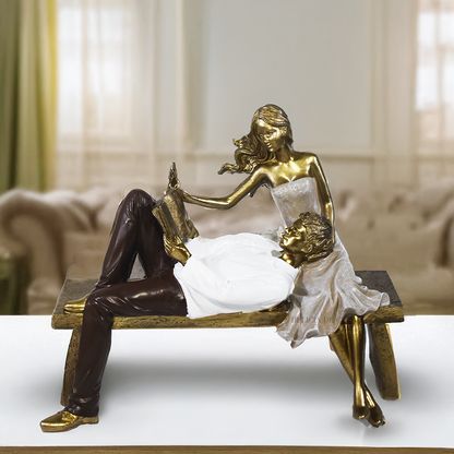 Escultura decorativa de casal romântico em resina sentados em um banco, com acabamento dourado, branco e marrom, simbolizando amor, cumplicidade e momentos especiais. 22,5x13x18 cm.