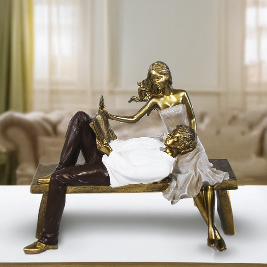 Escultura decorativa de casal romântico em resina sentados em um banco, com acabamento dourado, branco e marrom, simbolizando amor, cumplicidade e momentos especiais. 22,5x13x18 cm.