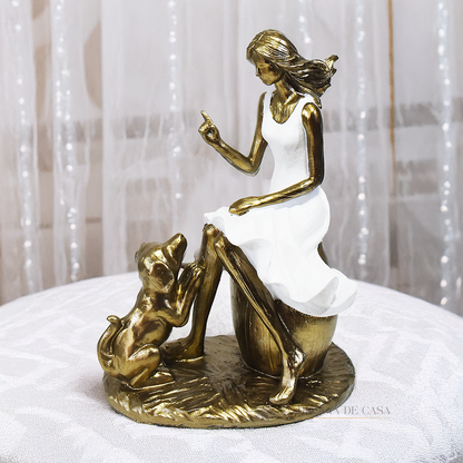 Escultura decorativa em resina de mulher sentada com cachorro em acabamento dourado para decoração de sala ou estante.