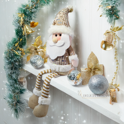 Boneco decorativo de Papai Noel sentado com pernas longas, roupas douradas e barba branca, ideal para decoração natalina em mesas e prateleiras.