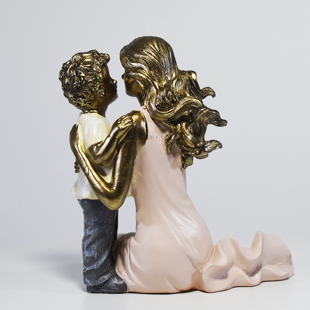 Escultura decorativa de mãe abraçando seu filho, confeccionada em resina com acabamento dourado, branco e cinza, medindo 11,5 x 11,5 x 8 cm.