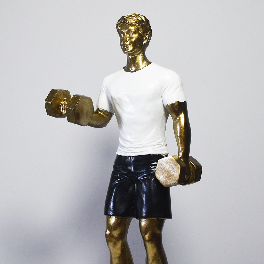 Escultura decorativa em resina representando atleta realizando exercício com halteres, com acabamento dourado, camiseta branca e shorts pretos.