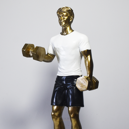 Escultura decorativa em resina representando atleta realizando exercício com halteres, com acabamento dourado, camiseta branca e shorts pretos.