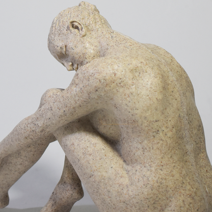 Escultura decorativa feminina em resina com acabamento que simula pedra natural, representando uma figura sentada em posição contemplativa.