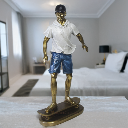Escultura decorativa em resina de mulher skatista sobre um skate, com acabamento dourado, branco e cinza.