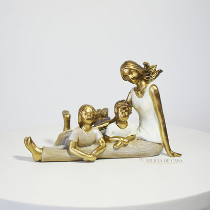 Escultura decorativa de mãe com dois filhos sentados, em resina dourada e branca, representando amor e união familiar.