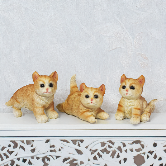 Três enfeites decorativos de gatinhos em resina em diferentes posições sobre fundo branco