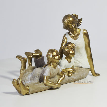 Escultura decorativa de mãe com dois filhos sentados, em resina dourada e branca, representando amor e união familiar.