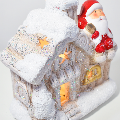 Casinha decorativa de Natal com Papai Noel e neve, feita em resina com glitter e luz interna, 12 cm de altura, nas cores bege, vermelho e cinza.