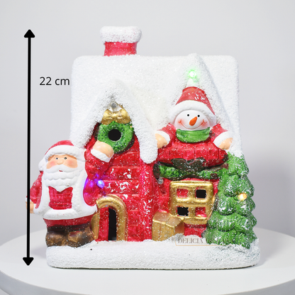 Casinha decorativa de Natal com Papai Noel, boneco de neve e árvore, feita em resina com glitter e luzes coloridas, 22 cm de altura.