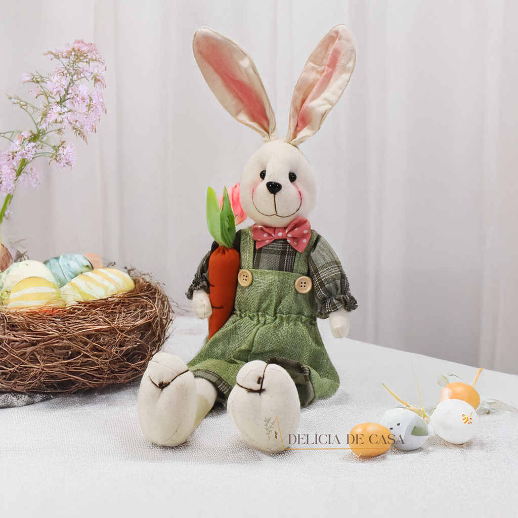 Dois coelhos de pelúcia sentados sobre um móvel, um vestindo macacão verde e segurando uma cenoura, e o outro com um vestido floral, ideal para decoração de Páscoa.