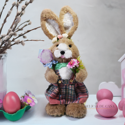 Coelho de pelúcia decorativo vestido com roupa social verde, segurando uma cenoura e uma enxada, ideal para decoração de Páscoa e ambientes rústicos.