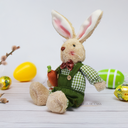 Coelho de pelúcia bege, vestido com macacão verde e camisa xadrez, segurando uma cenoura, ideal para decoração de Páscoa e ambientes temáticos.