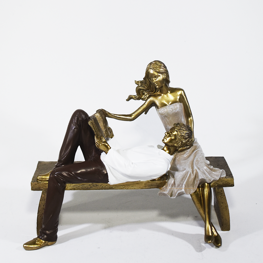 Escultura decorativa de casal romântico em resina sentados em um banco, com acabamento dourado, branco e marrom, simbolizando amor, cumplicidade e momentos especiais. 22,5x13x18 cm.