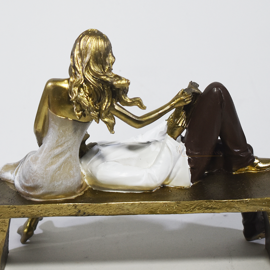 Escultura decorativa de casal romântico em resina sentados em um banco, com acabamento dourado, branco e marrom, simbolizando amor, cumplicidade e momentos especiais. 22,5x13x18 cm.