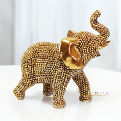 Escultura de elefante dourado coberto de strass, com tromba erguida e detalhes refinados, ideal para decoração luxuosa.