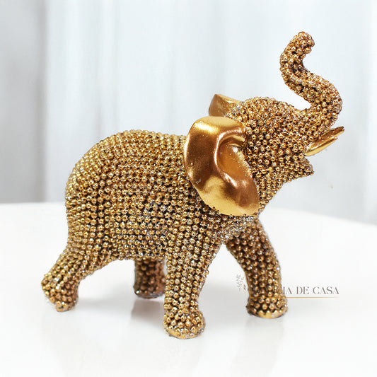 Escultura de elefante dourado coberto de strass, com tromba erguida e detalhes refinados, ideal para decoração luxuosa.