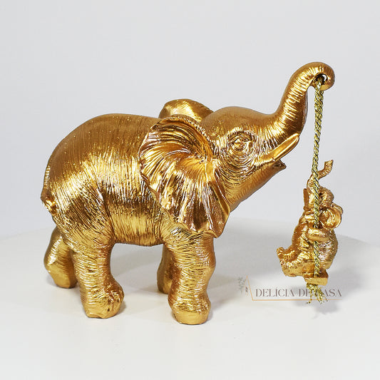 Escultura dourada de elefante mãe com tromba erguida segurando seu filhote por uma corda, representando amor e proteção.