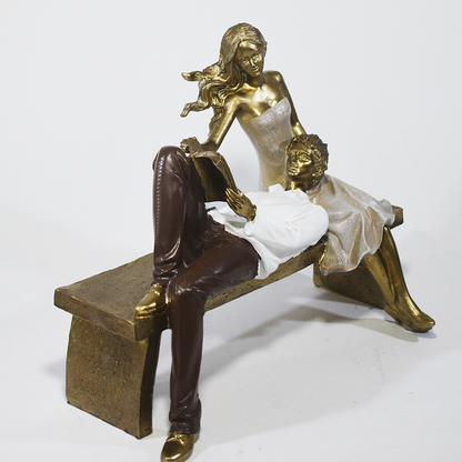 Escultura decorativa de casal romântico em resina sentados em um banco, com acabamento dourado, branco e marrom, simbolizando amor, cumplicidade e momentos especiais. 22,5x13x18 cm.