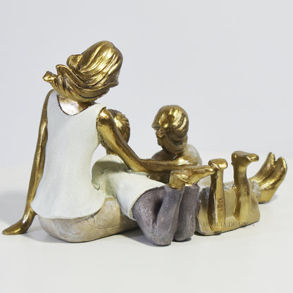 Escultura decorativa de mãe com dois filhos sentados, em resina dourada e branca, representando amor e união familiar.