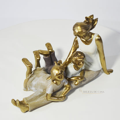 Escultura decorativa de mãe com dois filhos sentados, em resina dourada e branca, representando amor e união familiar.